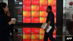 Para pengunjung melintas di depan layar yang menunjukkan data perdagangan Bursa Efek Indonesia (IDX), di Jakarta, 9 Maret 2020. (Foto: AFP)