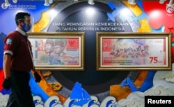 Seorang pria bermasker pelindung dan face shield berjalan melewati gambar uang pecahan tujuh puluh lima ribu rupiah di dinding, di Kantor Pusat Bank Indonesia, Jakarta, 2 September 2020. (Foto: REUTERS/Ajeng Dinar Ulfiana)