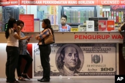 Sejumlah pelanggan mengecek nilai tukar ringgit Malaysia di sebuah penukaran mata uang asing di Kuala Lumpur, Malaysia, 24 Agustus 2015. (Foto: Vincent Thian/AP Photo)